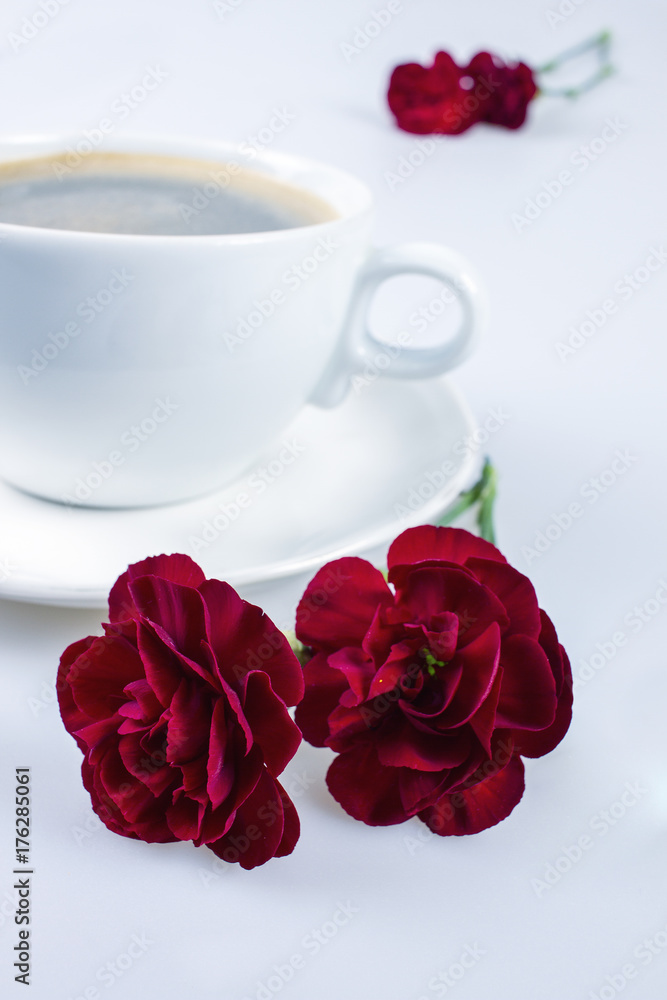 Coffee in an elegant cup and red carnations on white Coffee in an elegant cup and red carnations on white