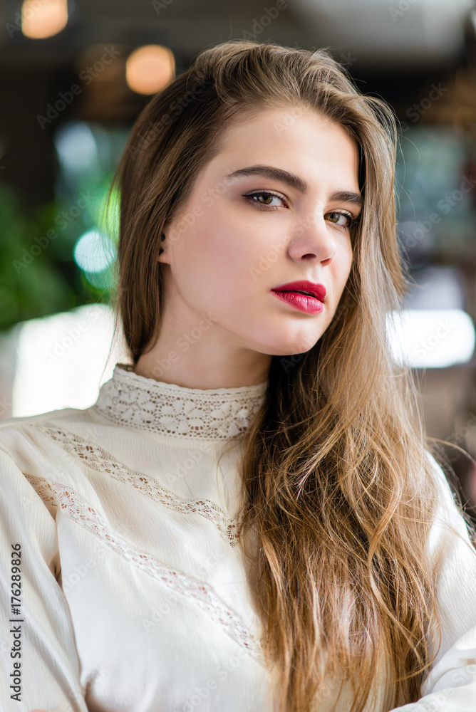 Fototapeta premium Beautiful young girl with professional makeup and hairstyle sitting in restaurant.