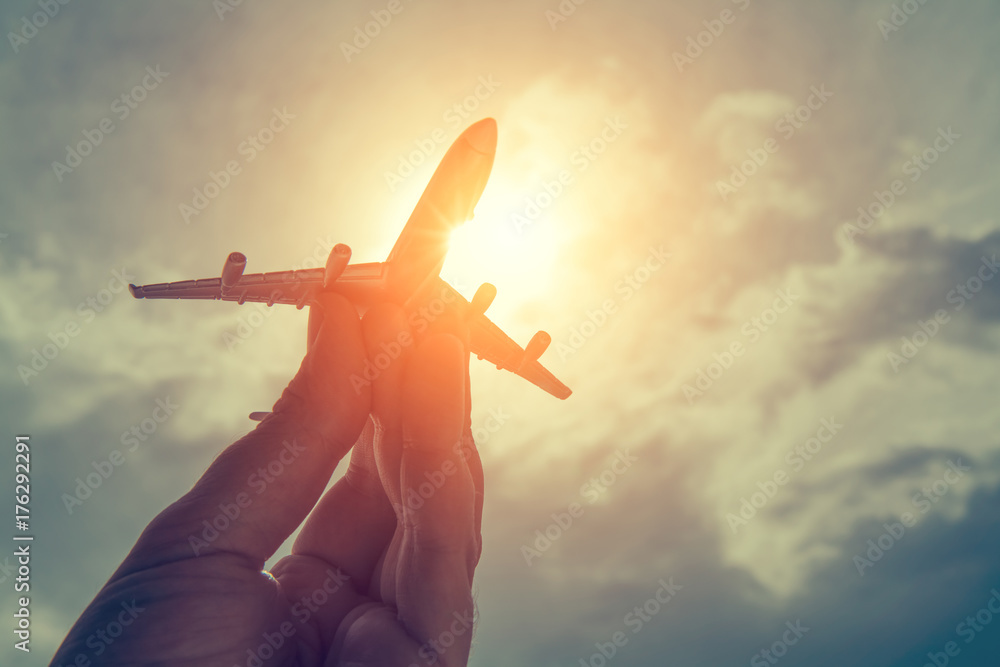 Naklejka premium ręka trzyma model samolotu przed pochmurnego nieba tle. koncepcja transportu lotniczego.