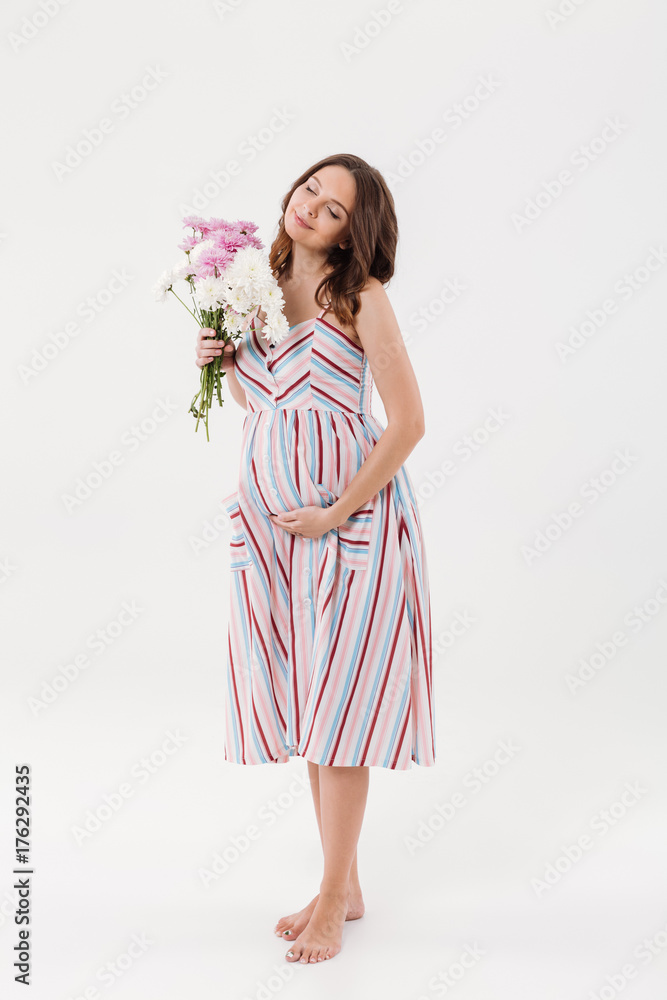 Cheerful pregnant woman holding flowers with eyes closed.