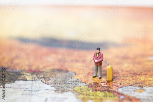 Business and travel concept. Businessman miniature figure with yellow luggage standing on world map.