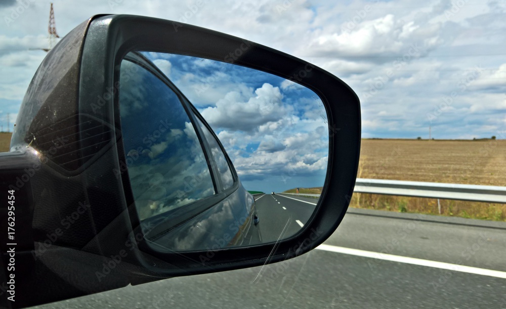 Rear view mirror reflecting road and cloudy sky