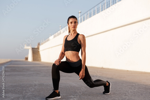 Young healthy lady stretching legs and making exercises near sea