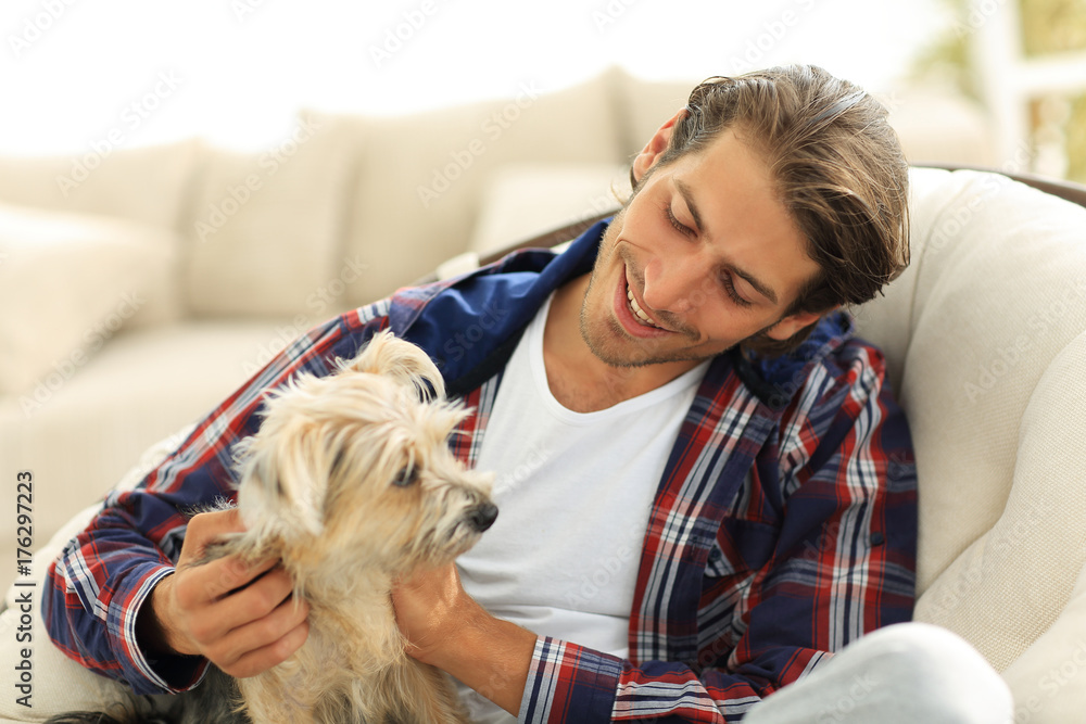 handsome guy stroking his dog while sitting in a large armchair. handsome guy stroking his dog while sitting in a large armchair.
