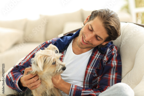 handsome guy stroking his dog while sitting in a large armchair.