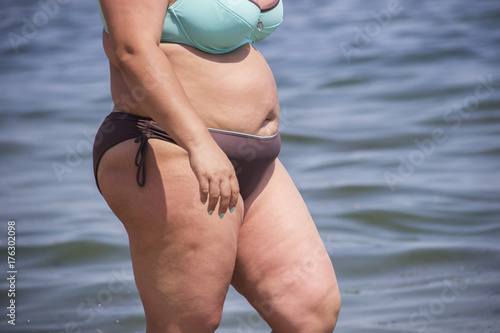 Overweight young woman in swimsuit near the sea, looking at the water, enjoys the hot sun in his summer holiday. photo