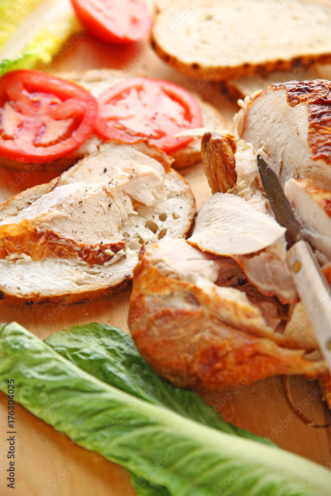 Cutting roast chicken into slices for sandwiches with lettuce and tomatoes
