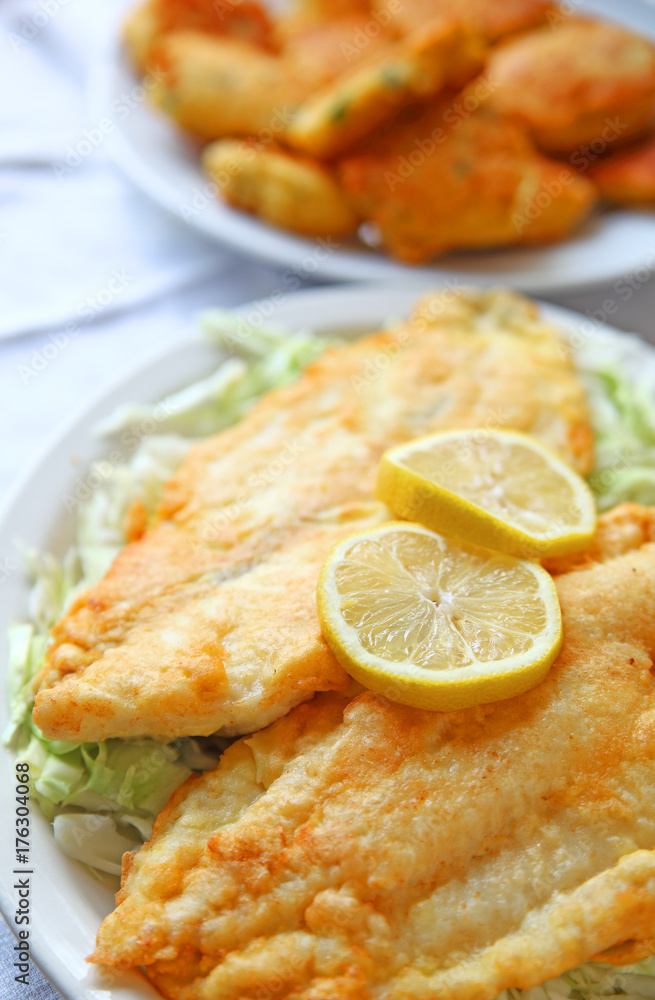 Battered and deep-fried catfish fillets on shredded cabbage with hushpuppies in the background Battered and deep-fried catfish fillets on shredded cabbage with hushpuppies in the background