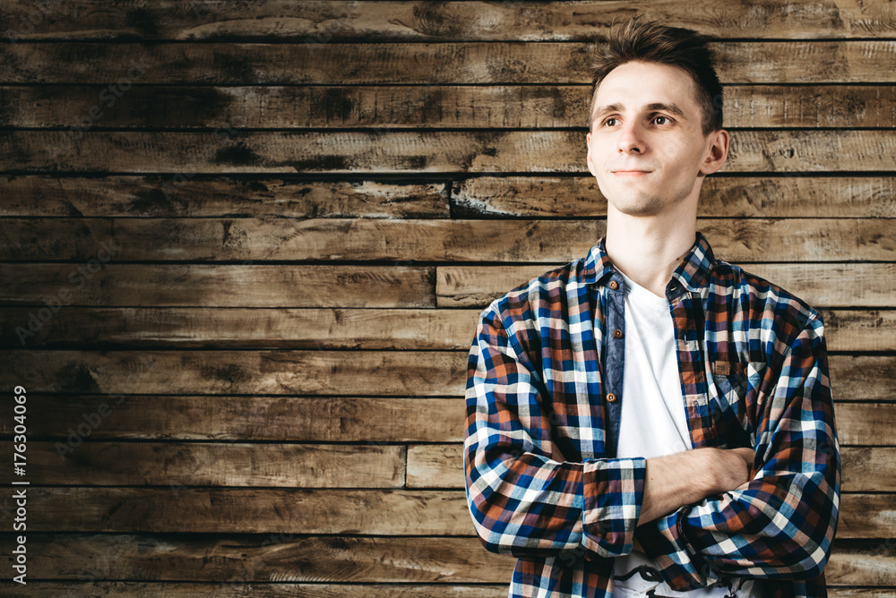 Happy attractive young man in plaid shirt standing and smiling over wooden background Happy attractive young man in plaid shirt standing and smiling over wooden background