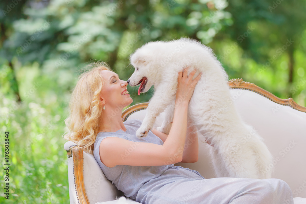 Beautiful young girl with a white puppy in her arms on a retro sofa in a summer garden Beautiful young girl with a white puppy in her arms on a retro sofa in a summer garden