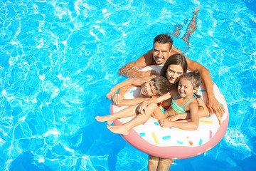 Happy family with inflatable ring relaxing in swimming pool