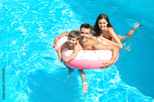 Young couple and cute son with inflatable ring in pool