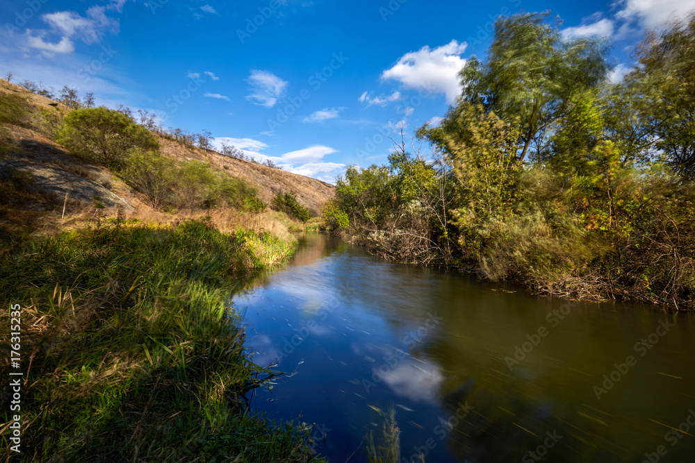 Early autumn landscape. Wild river flowing along the banks, densely overgrown with bushes and trees. Early autumn landscape. Wild river flowing along the banks, densely overgrown with bushes and trees.