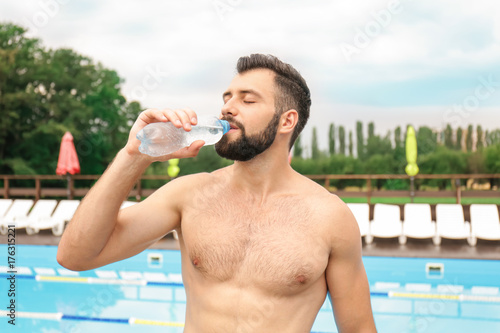 Handsome young man drinking water near swimming pool