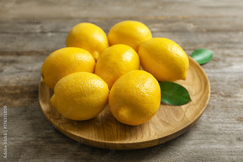 Plate with fresh lemons and leaves on wooden table Plate with fresh lemons and leaves on wooden table