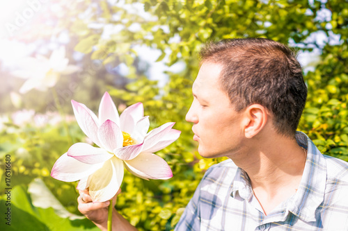 Portrait closeup of young man looking at bright white and pink lotus flower with yellow seedpod inside photo