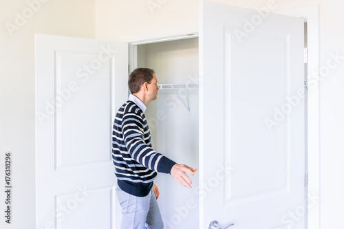 Young man checking looking inside small closet in new room after or before moving in, during open house