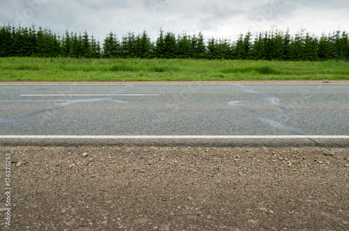 Highway.
Horizontal frame. Asphalt road with white marking is seen from the side, surrounded by green fields and forest