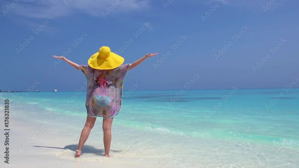 Woman in straw yellow sunhat walking along the beach Woman in straw yellow sunhat walking along the beach