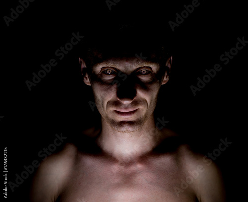 Stylish dark portrait of caucasian man who looks straight at you and looks like maniac. Expressive eyes.