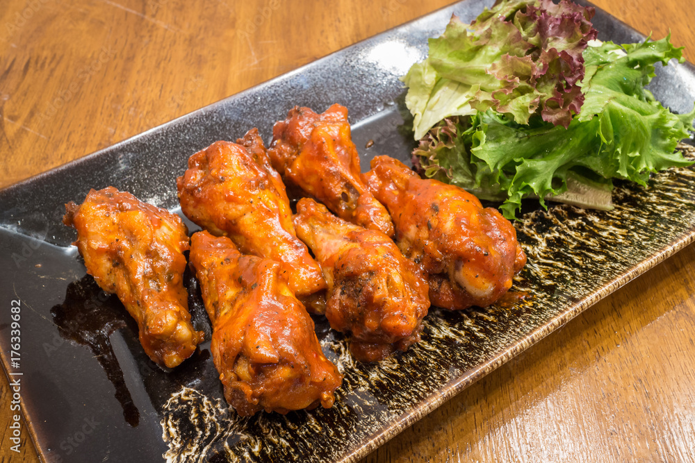 Healthy barbecue chicken wings with salad in a black dish on wood table background for ready to serve.