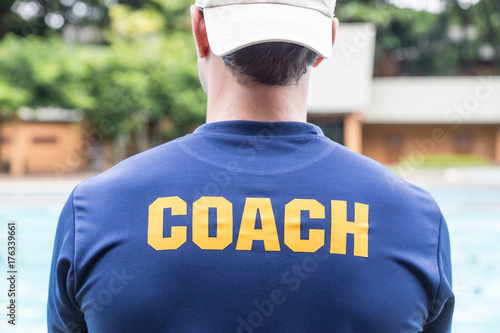 back of a sport coach's blue shirt with the yellow Coach word written on it