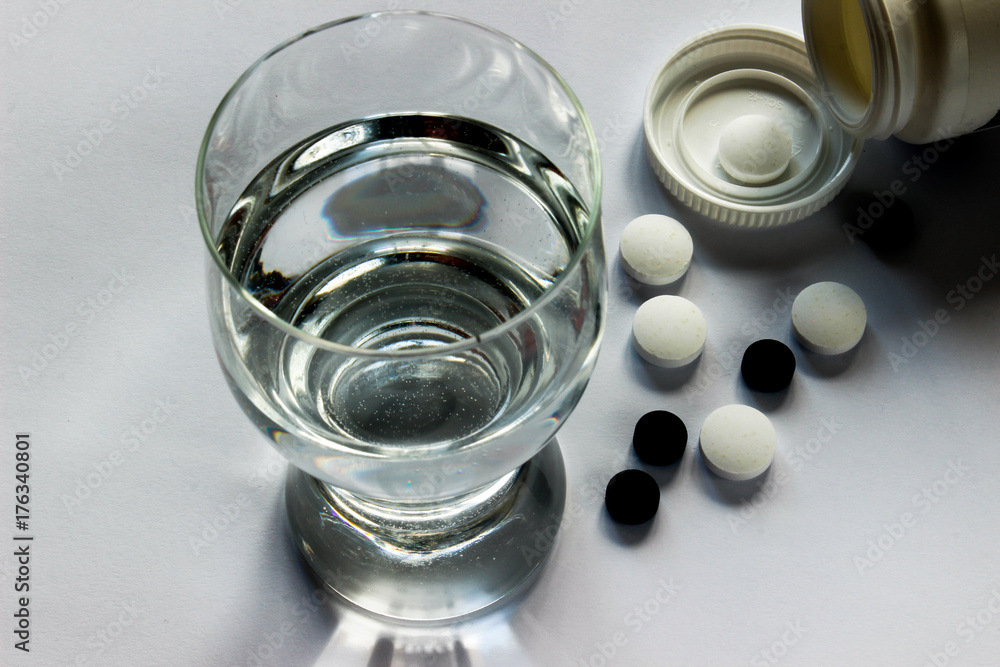 A glass of water and tablets on a white surface. A glass of water and tablets on a white surface.