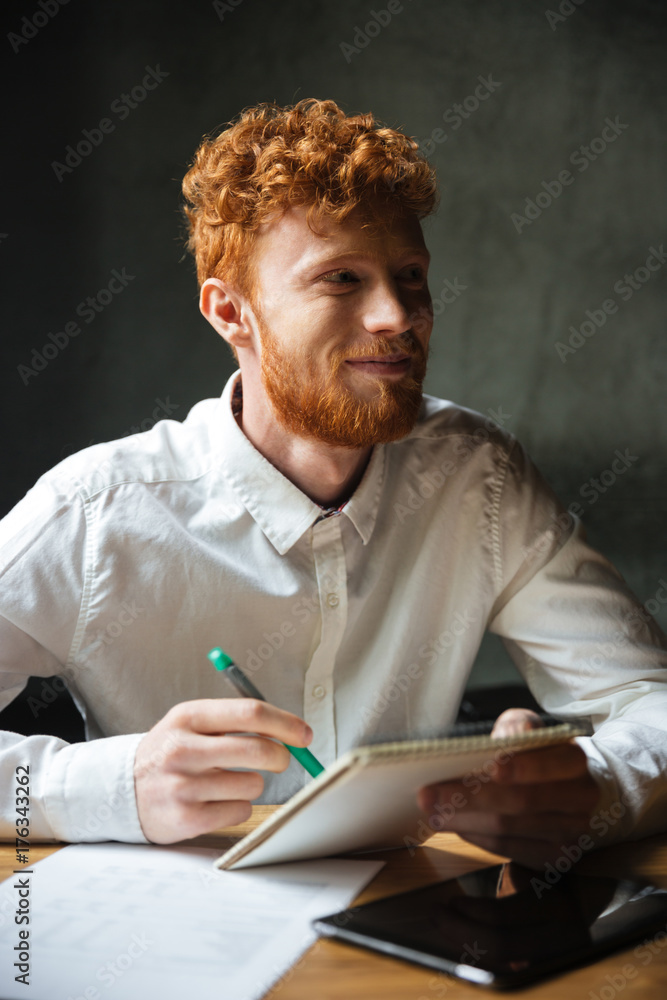 Close-up portrait of young readhed smiling student studying at home, looking aside Close-up portrait of young readhed smiling student studying at home, looking aside