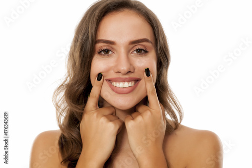Portrait of beautiful young woman forced her smile with her fingers on white background