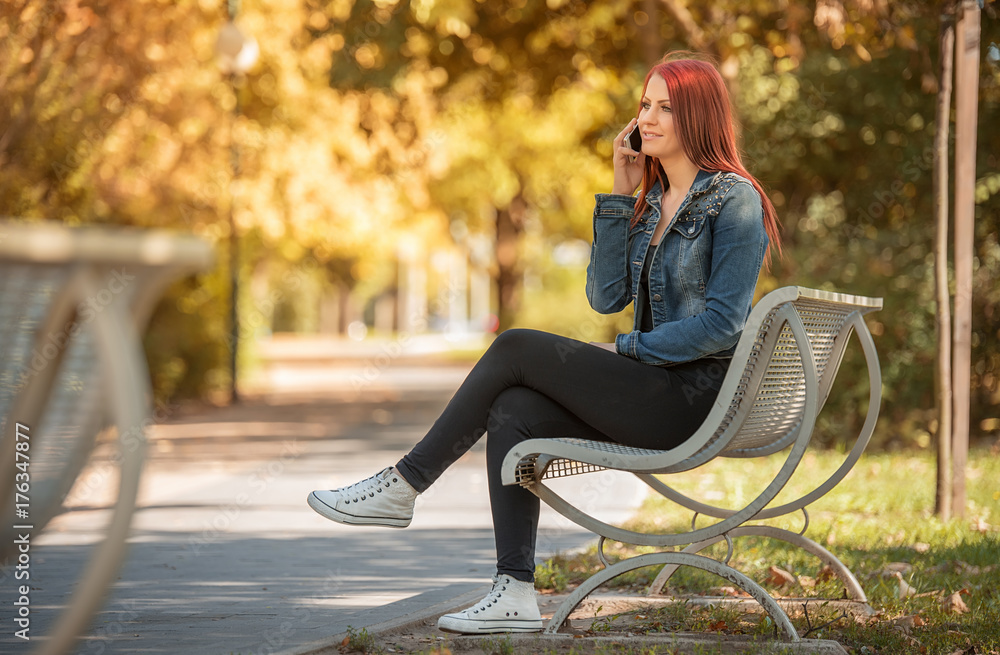 Charming woman sitting in park and call someone with phone Charming woman sitting in park and call someone with phone