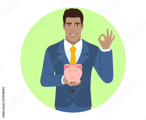 Businessman holding a piggy bank and showing a okay hand sign