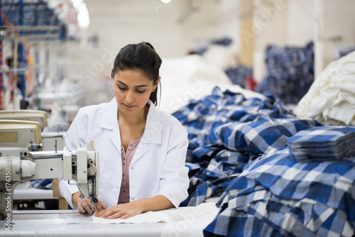 Skilled young tailor sewing on machine photo