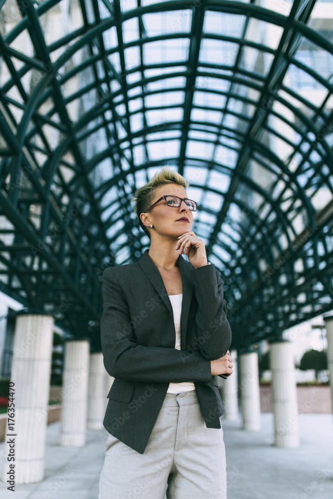 Fototapeta premium Young happy business woman standing in front of big modern building. She smiling and talking on her cell phone.