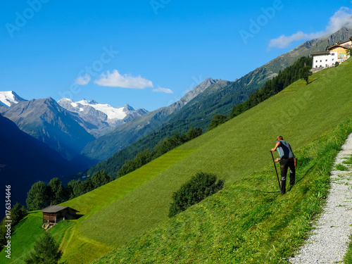 Bauer mit Sense vor Gebirgslandschaft