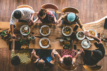 Group of friend pray before having nice food and drinks, enjoying the party and communication, Top view of Family gathering together at home for eating dinner.