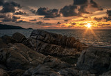 Seascape of sunset at sea with bright sun, cloudy sky and rocks at front