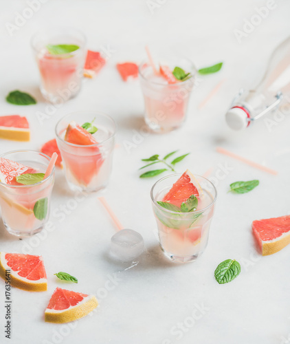 Flat-lay of cold refreshing summer alcohol cocktail with fresh grapefruit, mint and ice in glasses over white marble background, selective focus