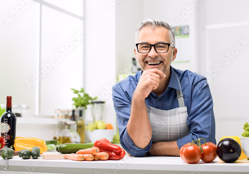 Smiling man posing in the kitchen, he is preparing healthy homemade food using fresh organic vegetables