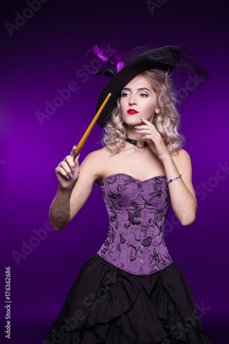 Beautiful woman, blonde in a good witch costume on a purple background holds a magic wand. Costume party, young girl. Halloween