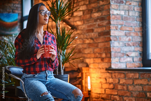 A woman drinks coffee in a room with loft interior.