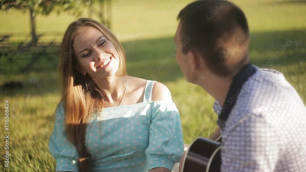 Young beautiful couple smiling, resting in park. Man playing guitar. Young beautiful couple smiling, resting in park. Man playing guitar.