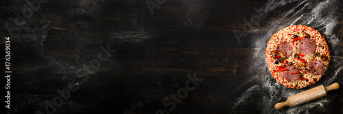 Girl hands making, decopating, preparing pizza with basil leaves on dark background. Top view, copy space. Banner