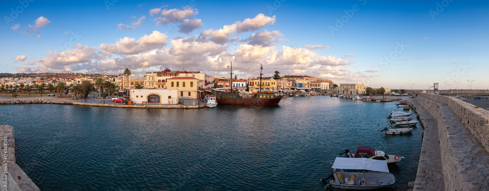 Venetian Harbour panorama with boats in front of restaurants at sunrise under colored clouds. Rethymno, Greece