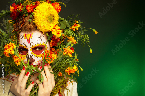 Fototapeta Naklejka Na Ścianę i Meble -  Женщина с разрисованным лицом к мексиканскому Дню Мертвых с цветами на зеленом фоне.