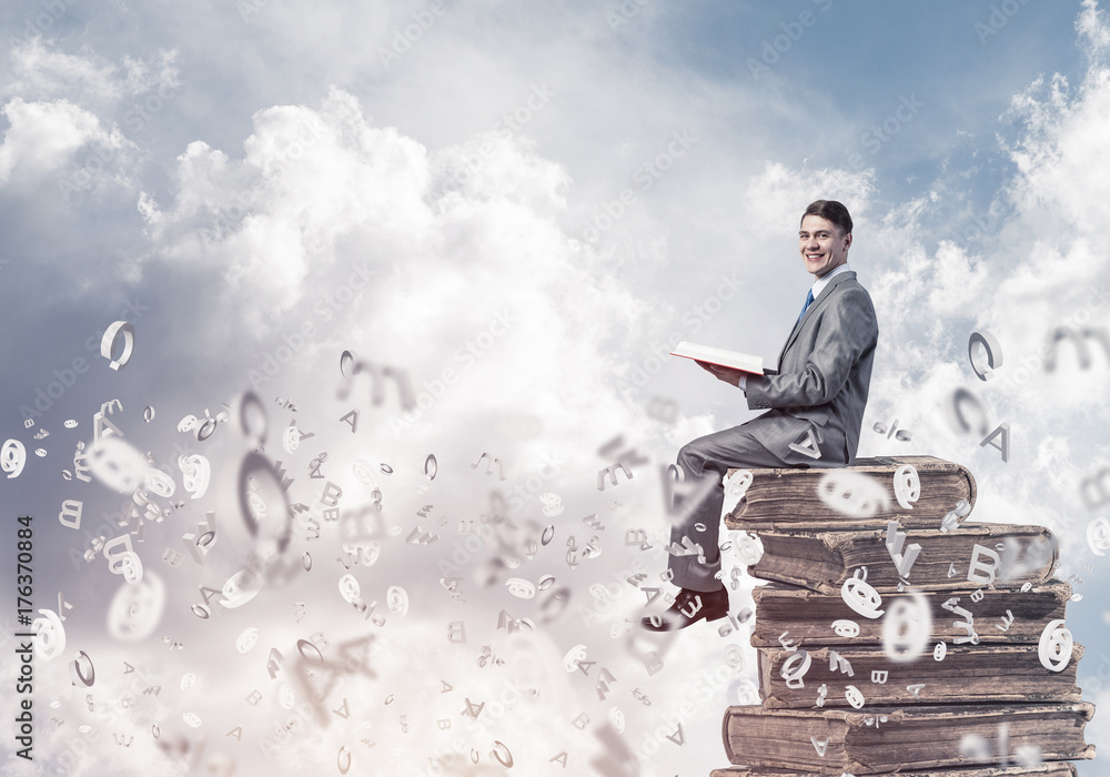 Man student on stack reading book and symbols flying around