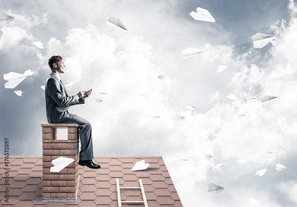 Man on brick roof send message with smartphone and paper planes 