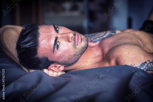 Valokuva Shirtless sexy muscular male model lying alone on his bed in his bedroom, lookin