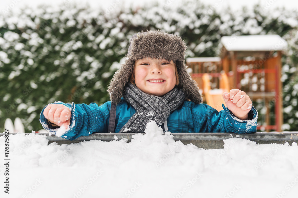 Adorable kid boy playing in sandbox full of snow, wearing warm hat Adorable kid boy playing in sandbox full of snow, wearing warm hat