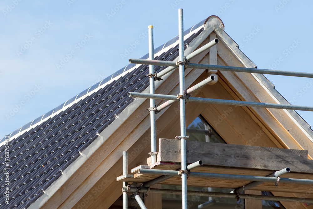 Naklejka premium Modern house roof construction. Black curved ceramic tiles with scaffolding.