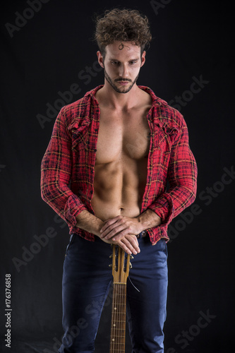 Studio portrait of handsome bearded man with unbuttoned shirt playing guitar over white background. Isolate.